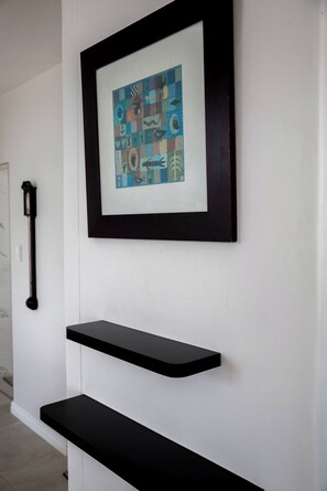 A framed artwork on a white wall above a black shelf. - Luxurious 3-bedroom Apartment With Ocean Views in Cape Town (Cape Town)