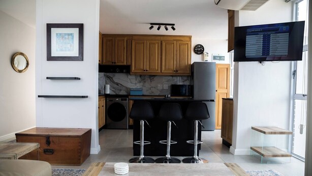 A modern kitchen with wooden cabinets, a built-in microwave, and a television displaying a program list. - Luxurious 3-bedroom Apartment With Ocean Views in Cape Town (Cape Town)