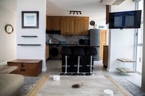 A modern kitchen with wooden cabinets, a built-in microwave, and a television displaying a program list.