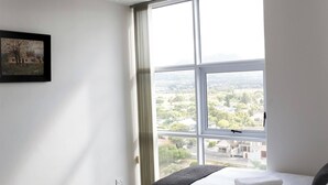 A hotel room with two beds, a ceiling fan, a large window with a city view, and a framed picture on the wall. - Luxurious 3-bedroom Apartment With Ocean Views in Cape Town (Cape Town)