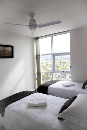 A hotel room with two beds, a ceiling fan, a large window with a city view, and a framed picture on the wall. - Luxurious 3-bedroom Apartment With Ocean Views in Cape Town (Cape Town)
