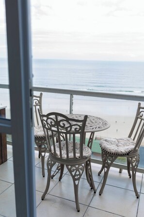 A balcony with a round table and four chairs, overlooking a beach. - Luxurious 3-bedroom Apartment With Ocean Views in Cape Town (Cape Town)