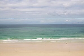 Ein weiter Strand mit ruhiger See, blauem Himmel und Bergen in der Ferne.