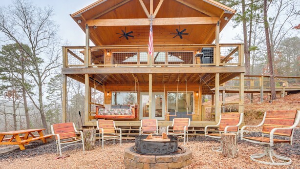 A two-story wooden cabin with a balcony, outdoor seating, and a fire pit. - Cabin on Beaver Lake w/ Views & Furnished Deck! (Rogers)