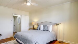 Ein Schlafzimmer mit Bett, Nachttisch, Stehlampe, Deckenventilator und einer Tür zu einem anderen Raum.