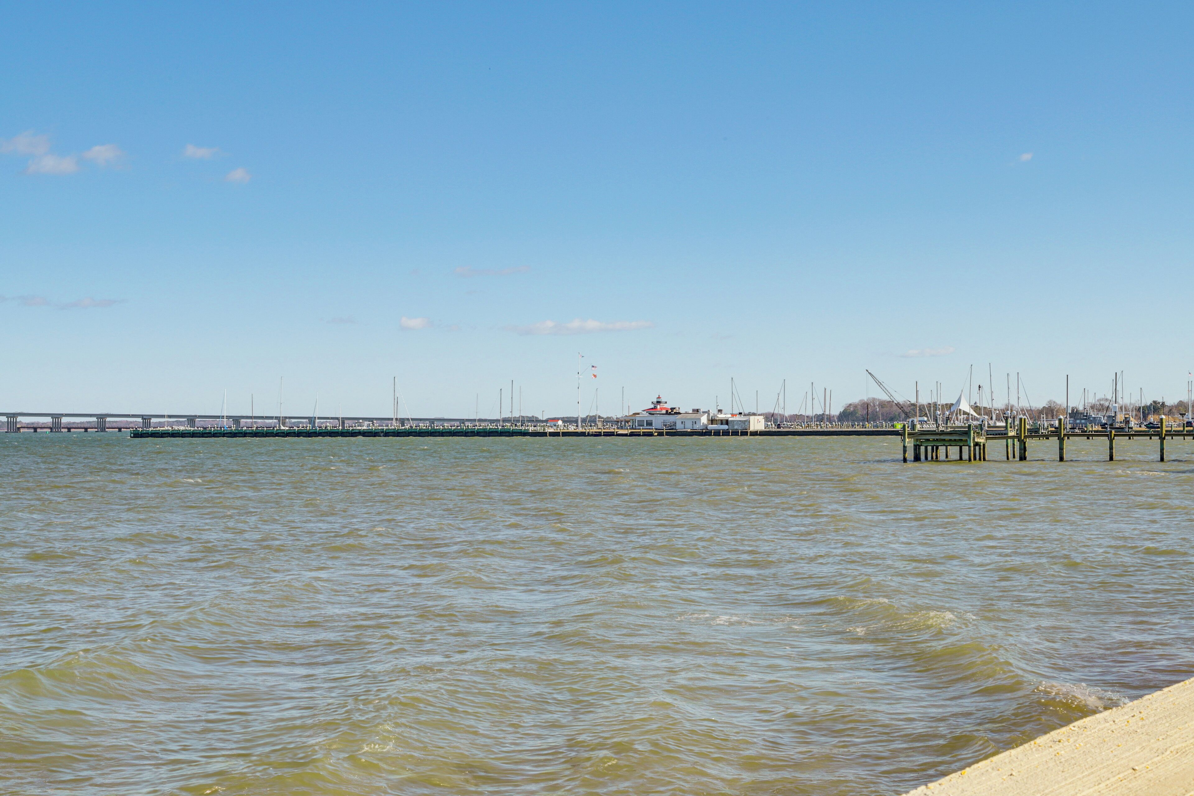 Blick auf das Wasser mit einer anlegenden Mole, einer Brücke im Hintergrund und einem klaren Himmel.
