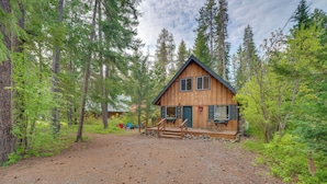 A cabin surrounded by tall trees, with a gravel driveway leading to a wooden deck. - 1 Mi to Lake Easton: Cozy Cascades Cabin! (Easton)