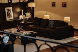 A modern living room with a dark-colored sofa, a coffee table with books and decorative items, and two wall-mounted lamps. - THELILY Designer Hotel (Chongqing)