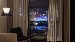 Habitación de hotel moderna con vistas a un paisaje urbano nocturno, con edificios iluminados y una masa de agua.