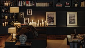 Un salón con decoración oscura, que incluye un sofá, una mesa de centro y una estantería llena de libros y objetos decorativos.