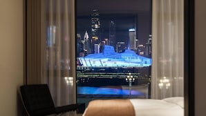 Una habitación de hotel con una cama, una silla y vista a un paisaje urbano nocturno.