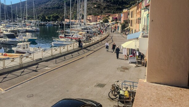 A marina with boats docked, a pedestrian walkway, and buildings along the waterfront. - Casa del porticciolo di Capraia (Porto)