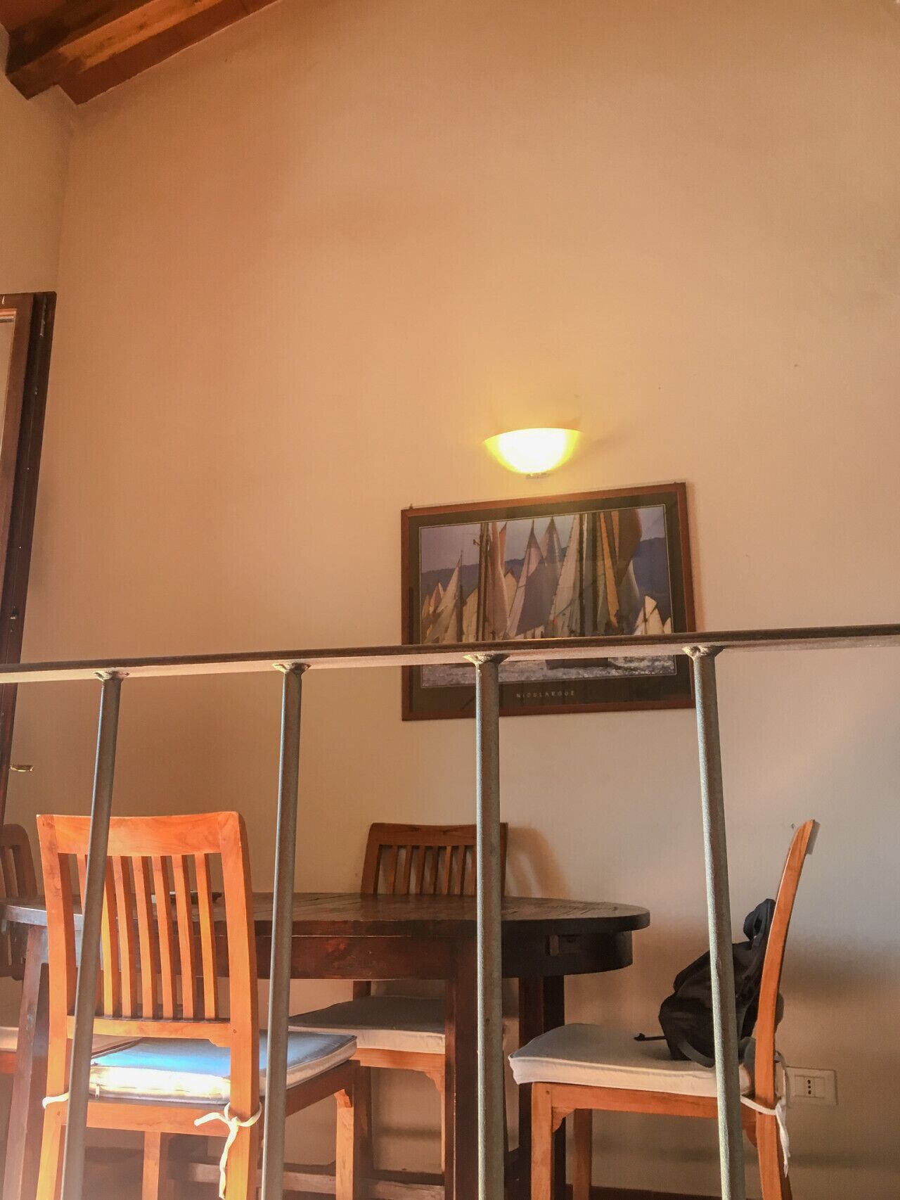 Un coin repas avec des chaises en bois et une table, un tableau accroché au mur et un luminaire au plafond.