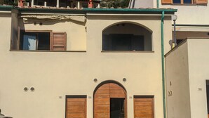 A building with a central arched entrance, two side doors, and a small balcony with a railing. - Casa del porticciolo di Capraia (Porto)