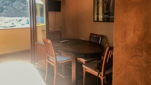 A dining area with a round table, chairs, a TV, and a view of a beach. - Casa del porticciolo di Capraia (Porto)