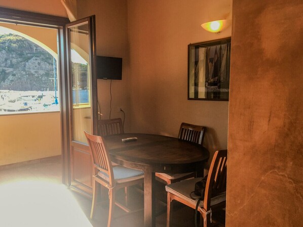 Un comedor con una mesa redonda, sillas, un televisor y vista a una playa.