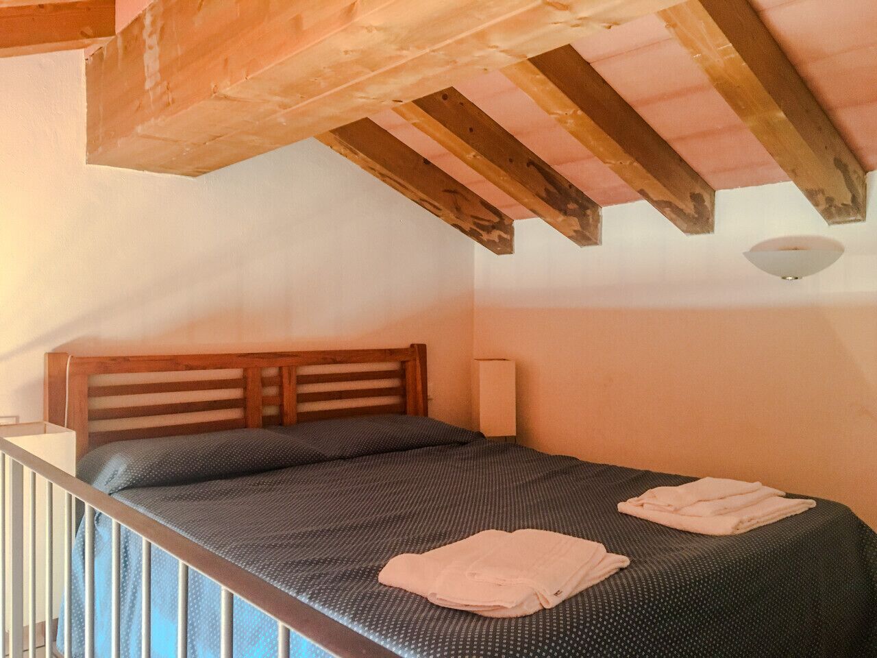 Una camera da letto con una testiera in legno, un letto singolo con copripiumino fantasia scura e due asciugamani piegati sul letto.