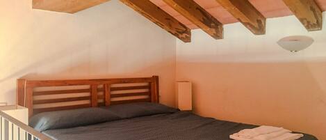 Una camera da letto con una testiera in legno, un letto singolo con copripiumino fantasia scura e due asciugamani piegati sul letto.