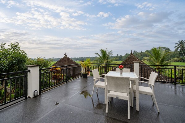 A covered outdoor area with a table and chairs, a small gazebo, and a view of a green landscape.