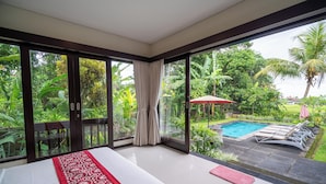 A bedroom with a large sliding glass door leading to a pool area, surrounded by lush greenery. - Mardika Private Villa Ubud (Ubud)
