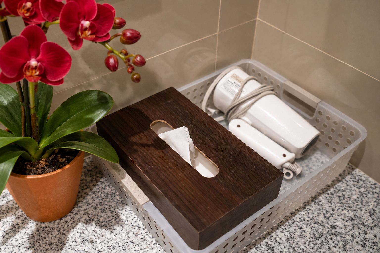 A bathroom with a wooden tray holding a white towel, a potted plant with red flowers, and a white basket containing toiletries.