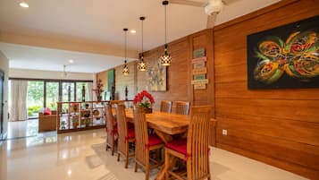 Un comedor con una mesa y sillas de madera, luces colgantes y un cuadro en la pared.