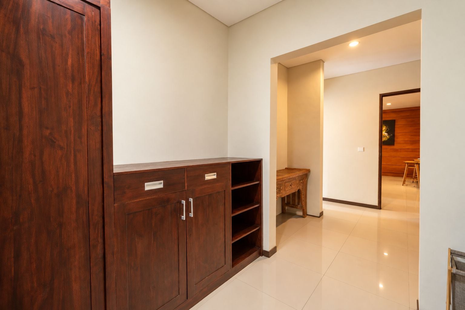 Un pasillo con un armario de madera, un escritorio de madera y un comedor con mesa y sillas de madera.