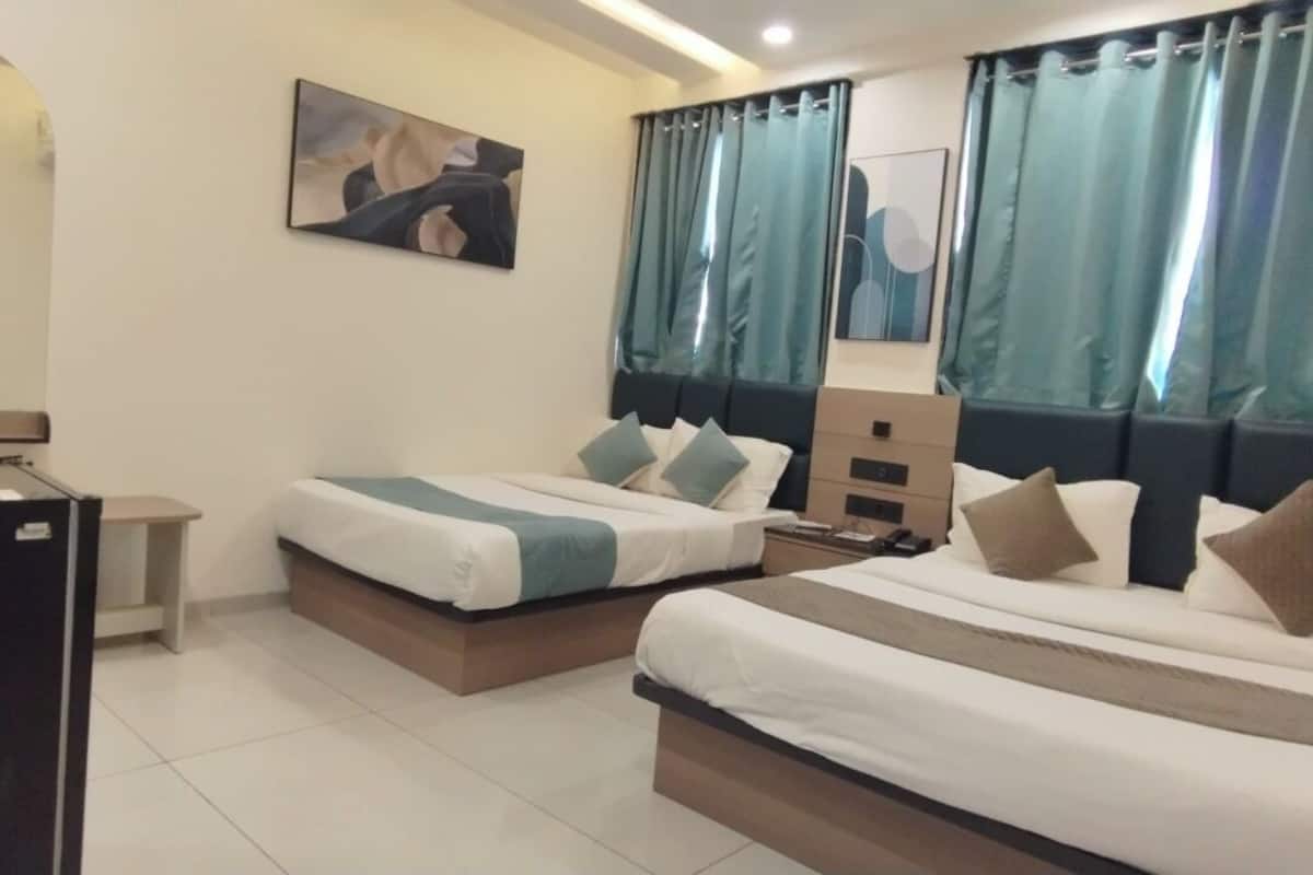 Una habitación de hotel con dos camas, un escritorio, un espejo y cortinas color turquesa.