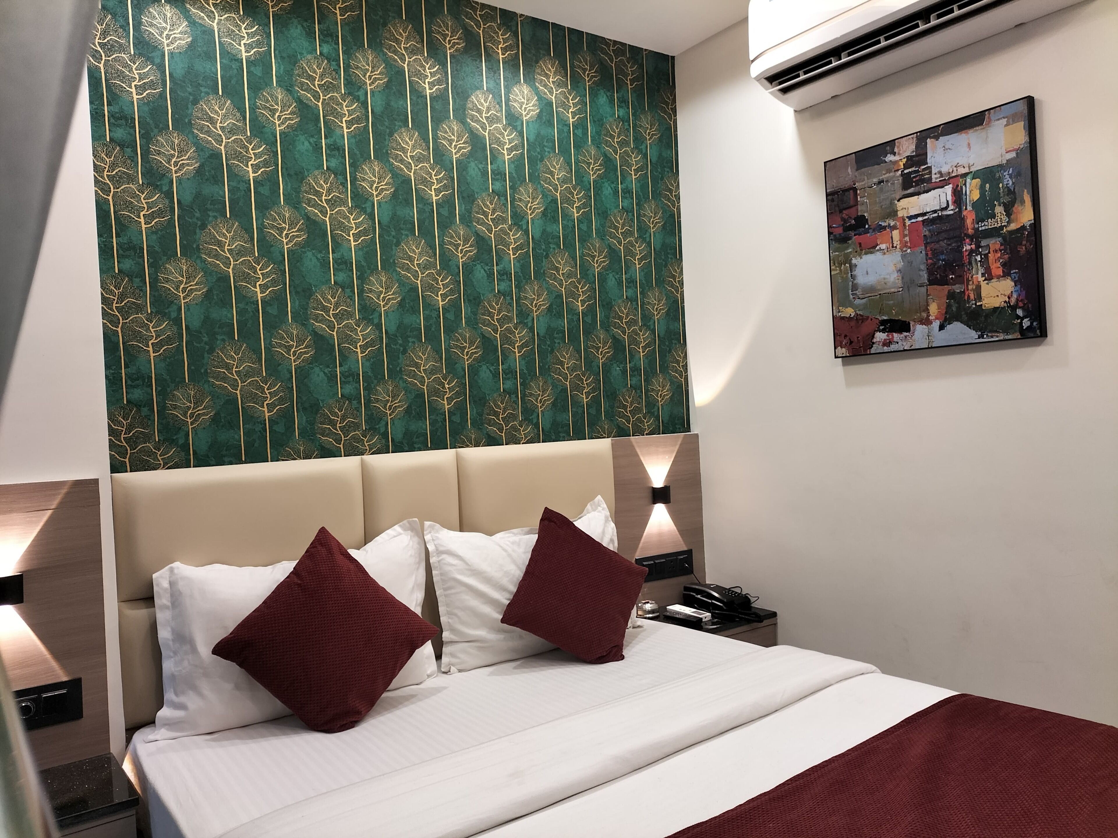 Hotelkamer met een bed, twee kussens, een nachtkastje, een wandairconditioner en een schilderij.