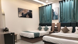 A modern hotel room with two beds, a small desk, a refrigerator, and a painting on the wall. - Hotel Paris Plaza (Ahmedabad)