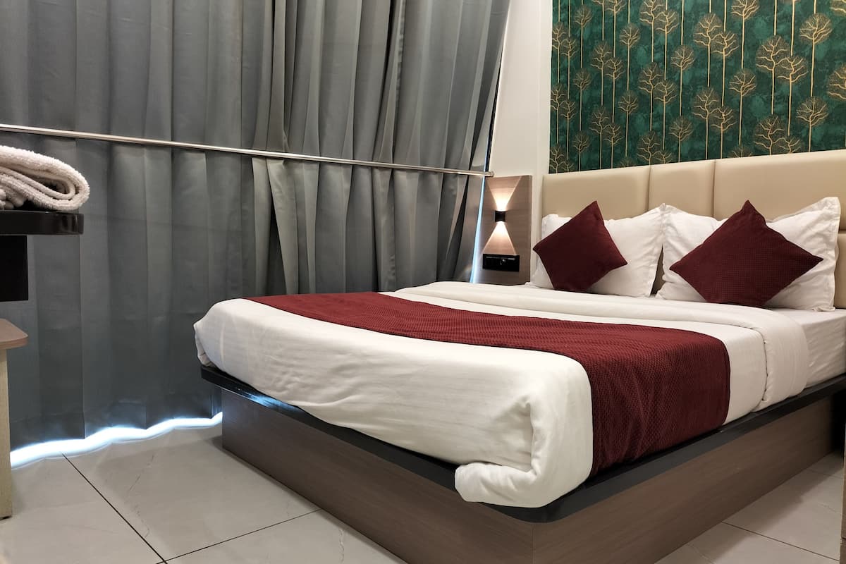 Una habitación de hotel moderna con una cama grande, cortinas grises, un toallero en la pared y un papel tapiz estampado.
