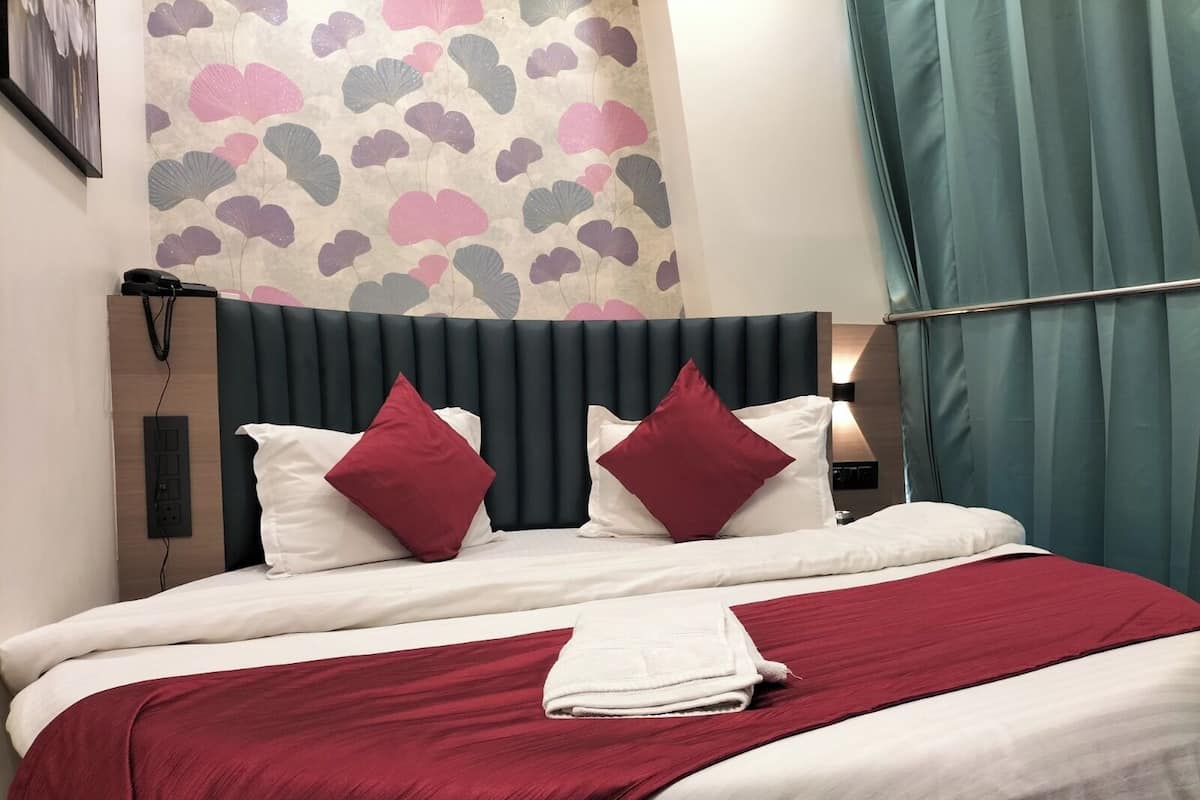 Una cama bien hecha con cabecera oscura, almohadas blancas y rojas, y una colcha roja.