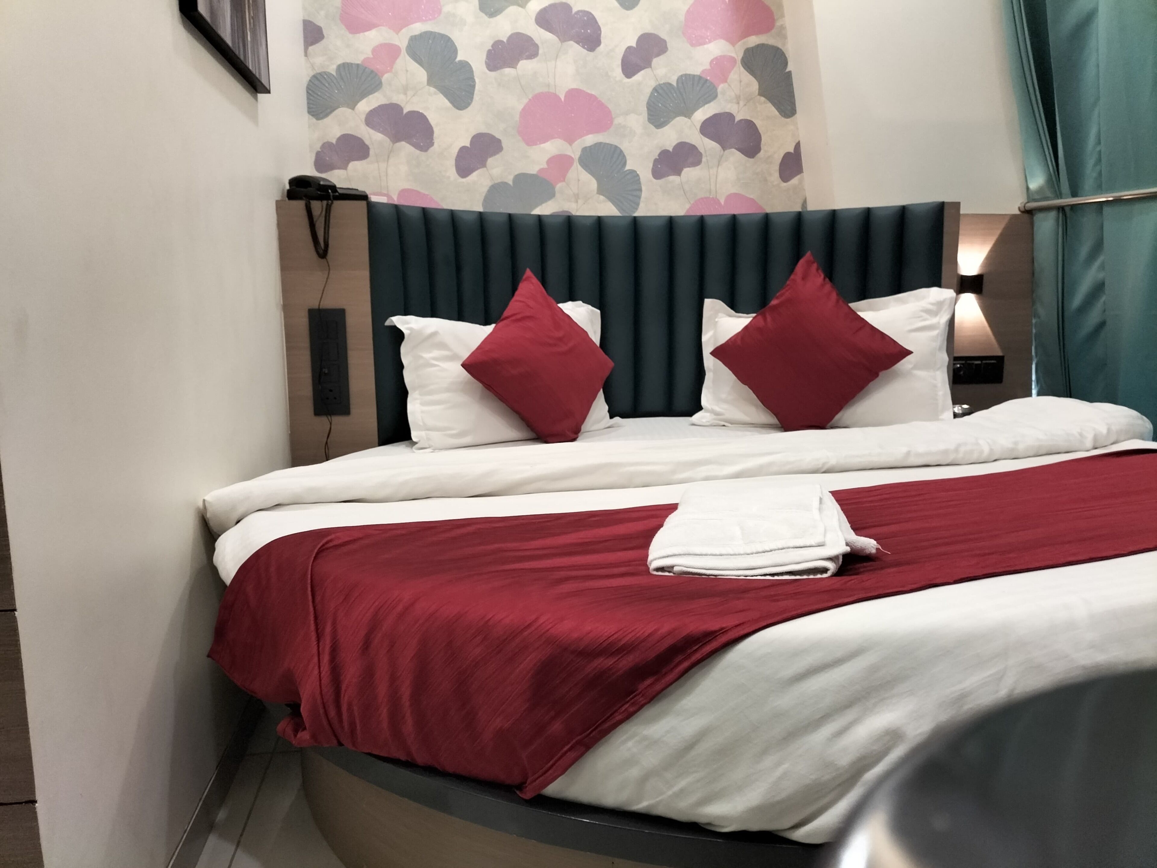 A neatly made bed with white and red bedding, a dark headboard, and a wall with a heart pattern.