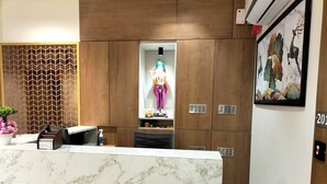 A hotel reception desk with a marble counter, wooden paneling, a decorative wall, and a framed artwork. - Hotel Paris Plaza (Ahmedabad)