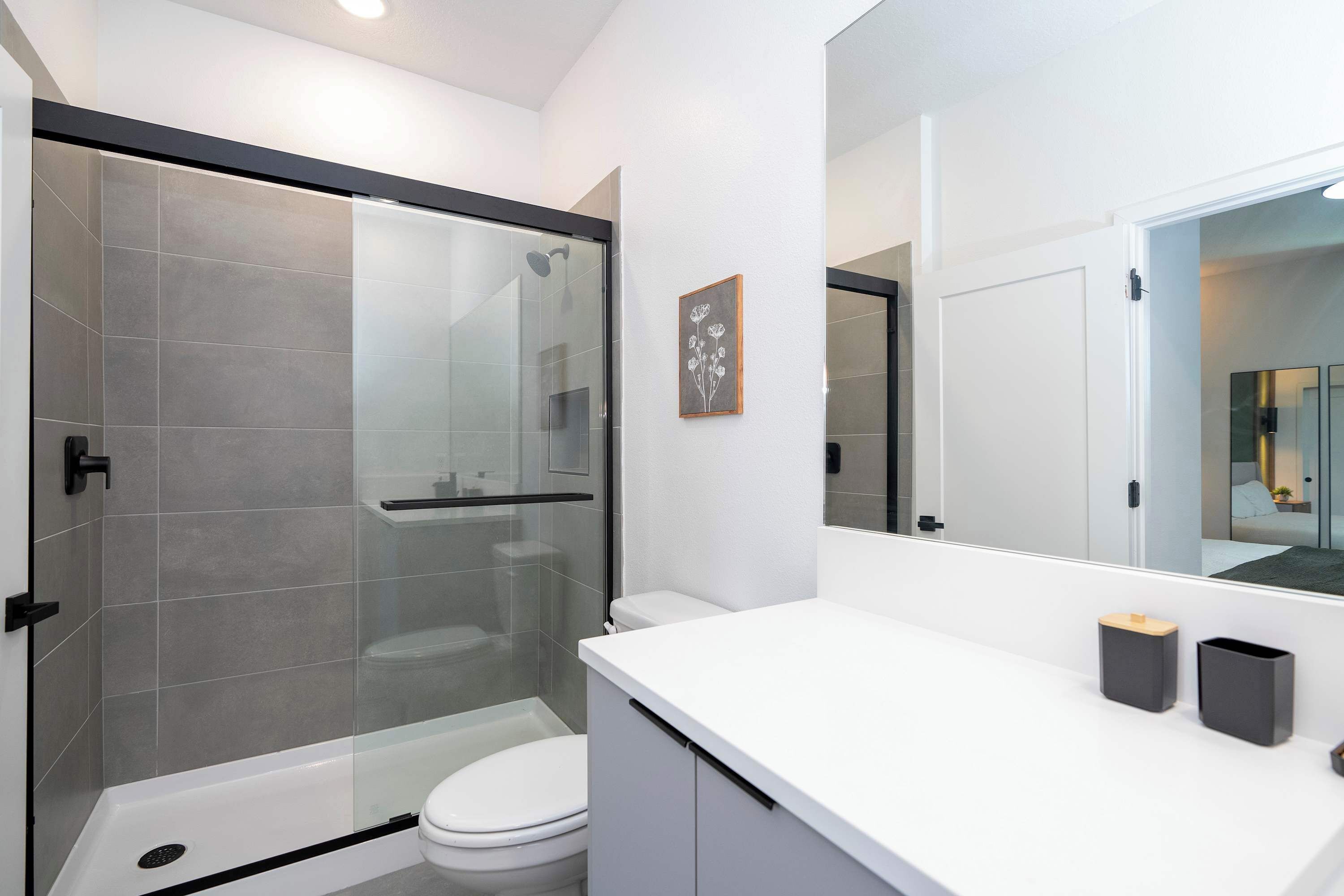 Un baño moderno con cabina de ducha de vidrio, inodoro blanco y tocador blanco con dos contenedores negros para almacenamiento.