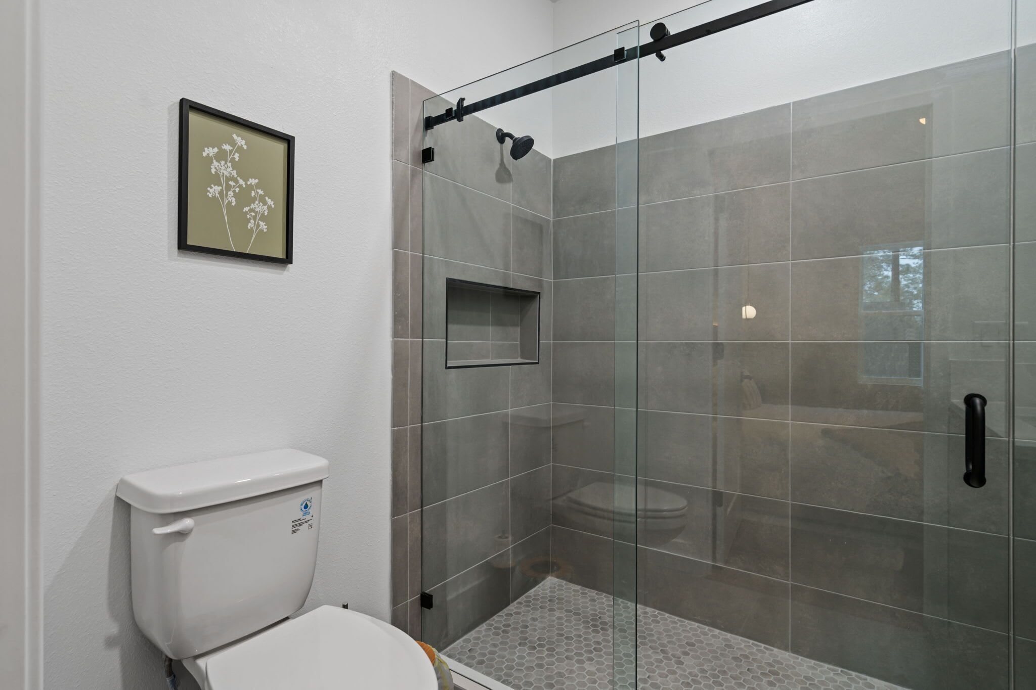 Un baño moderno con cabina de ducha de vidrio, inodoro y un cuadro en la pared.
