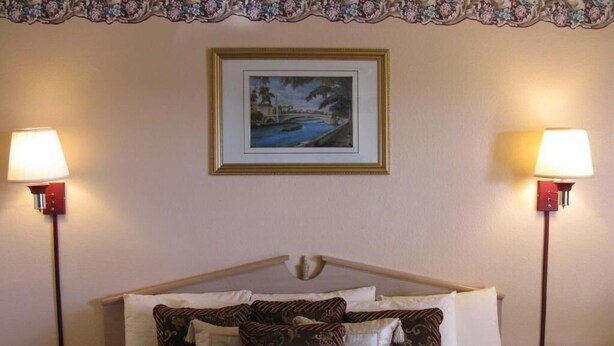 A hotel room with a bed, two bedside lamps, a framed picture on the wall, and a floral-patterned headboard. - Charming Hotel in a quiet spot, next to a Walmart, located in Seminole, Texas. (Seminole)
