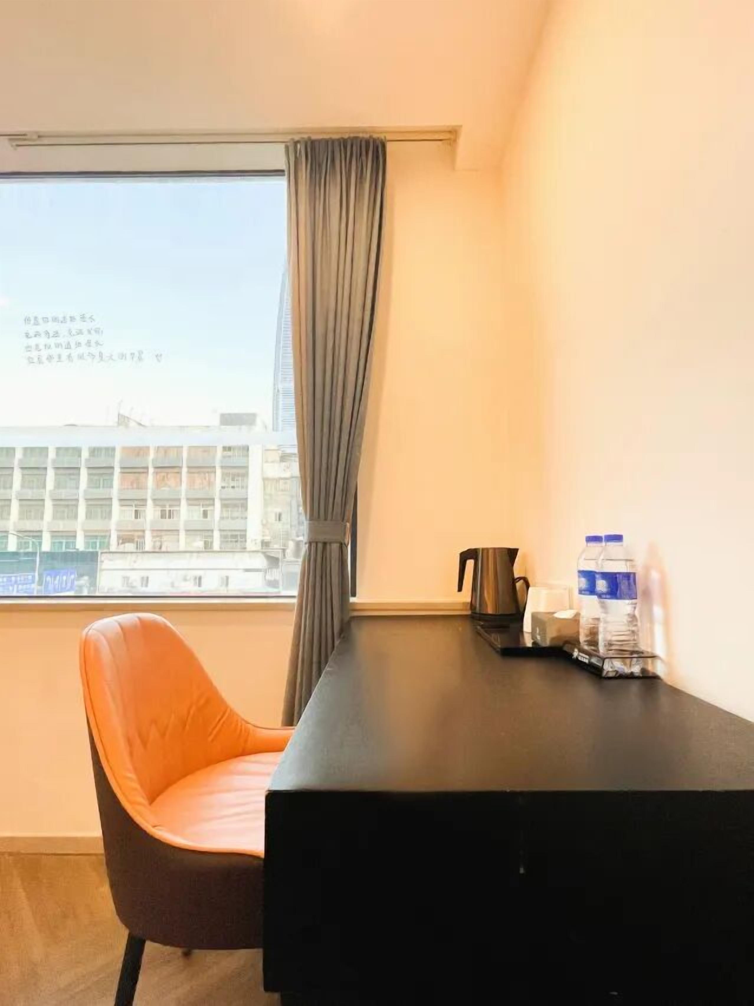 A hotel room with a single bed, a desk with a kettle, a chair, and a window with curtains.