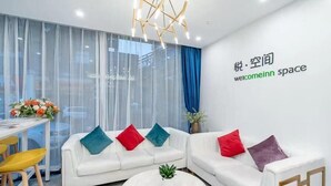 Un moderno vestíbulo de hotel con un conjunto de sofá blanco, una mesa de centro redonda y un amplio ventanal con cortinas translúcidas.