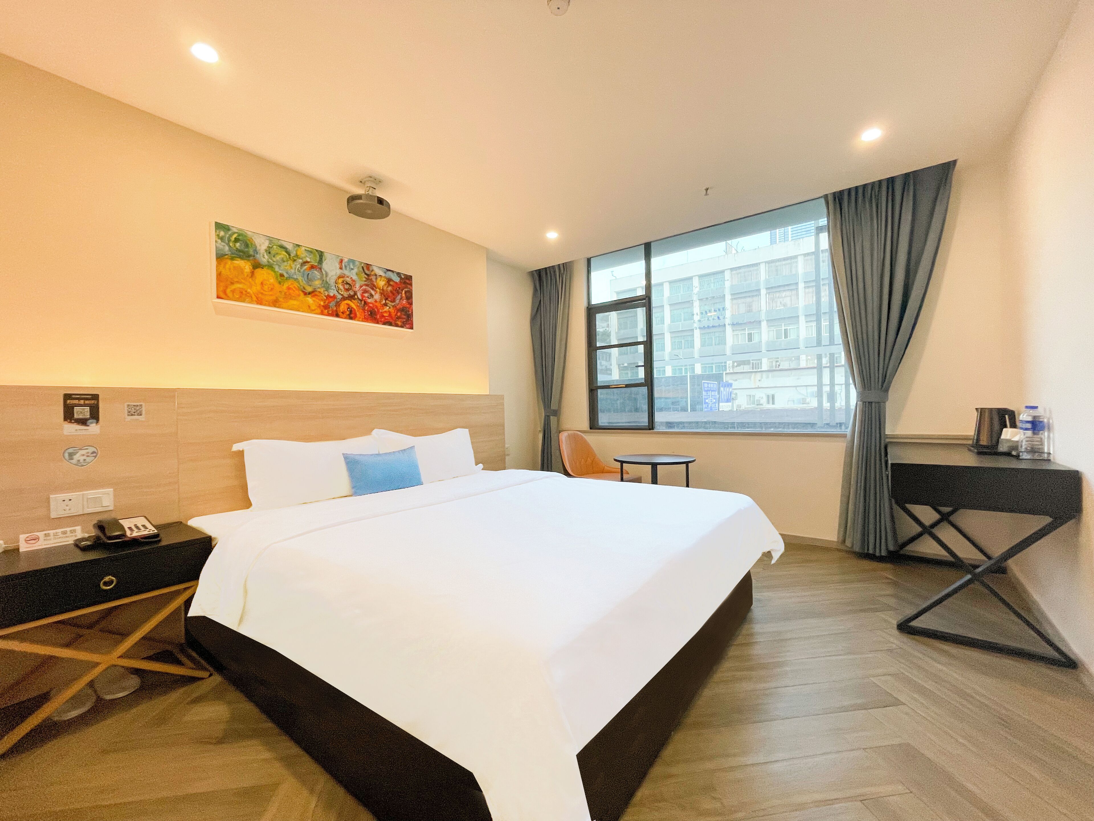 A hotel room with a large bed, a small table, a chair, a nightstand, and a painting on the wall.