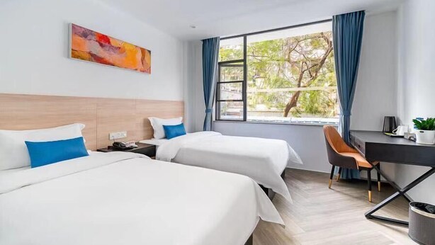Habitación de hotel con dos camas, un escritorio y una silla. Cuenta con ventana con cortinas, un cuadro en la pared y vistas a árboles.