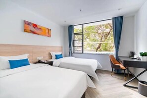 A hotel room with two beds, a desk, and a chair. There is a window with curtains, a painting on the wall, and a view of trees outside. - Shenzhen Welcome Inn (Shenzhen)