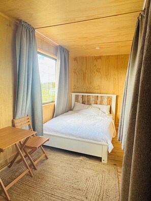 A bedroom with a bed, a wooden desk, a chair, and a window with curtains. - Ataahua HighlandA little slice of Paradise- Off Grid retreat. (Te Kopuru)