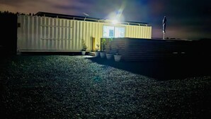 A modern building with a flat roof, large windows, and a small porch area with potted plants. - Ataahua HighlandA little slice of Paradise- Off Grid retreat. (Te Kopuru)
