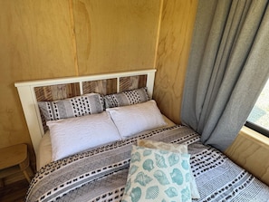 Un lit avec une literie à motifs et des oreillers, une tête de lit en bois et une fenêtre avec des rideaux.