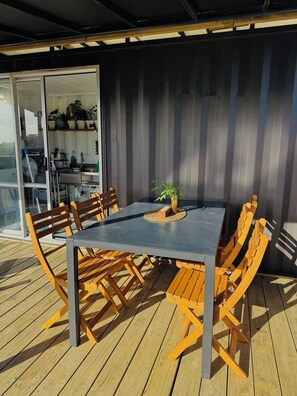 An outdoor dining area with a table and chairs, a small plant on the table, and a sliding glass door leading to a kitchen area. - Ataahua HighlandA little slice of Paradise- Off Grid retreat. (Te Kopuru)