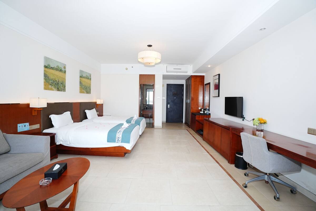 Habitación de hotel con cama, sofá, escritorio y una silla. Hay un televisor en el escritorio y un cubo de basura al lado.