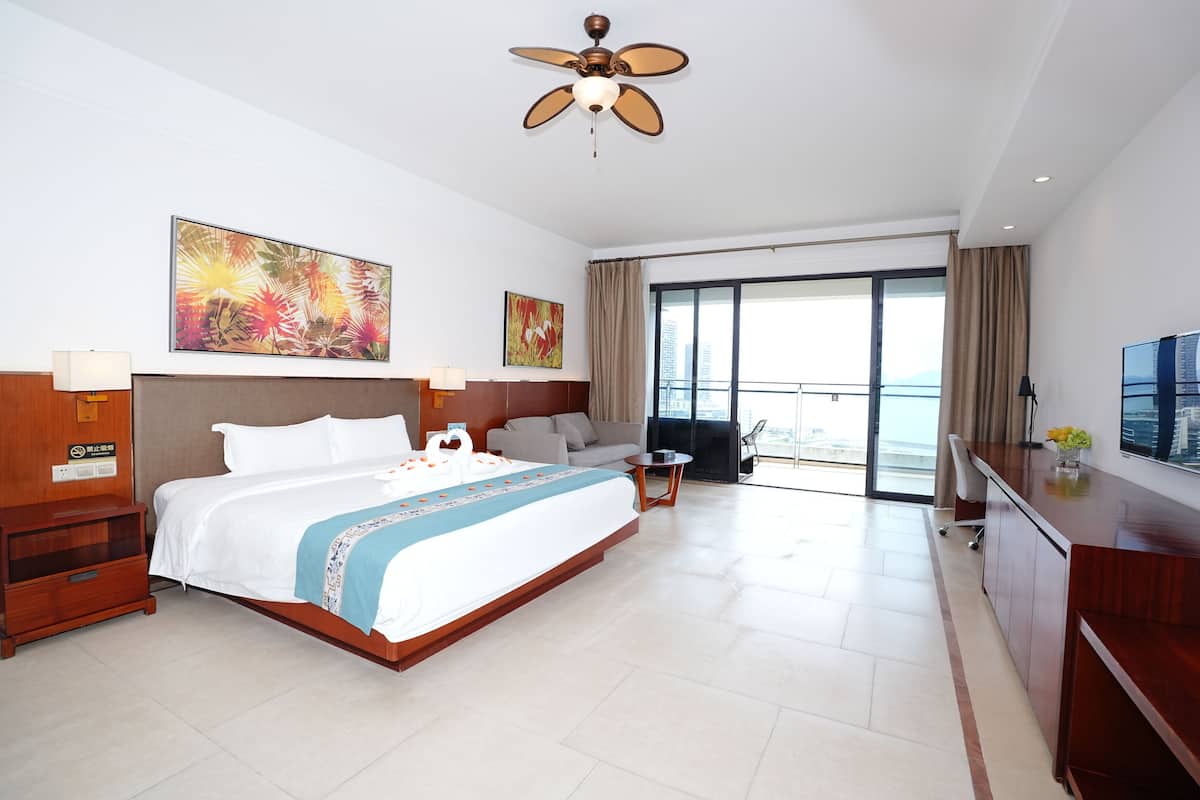 Habitación de hotel con una cama grande, un escritorio, una silla, un televisor y un balcón con vistas a la ciudad.