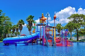 Un parque acuático con un tobogán azul, una estructura de escalada roja y una zona de juegos con forma de estrella de mar.