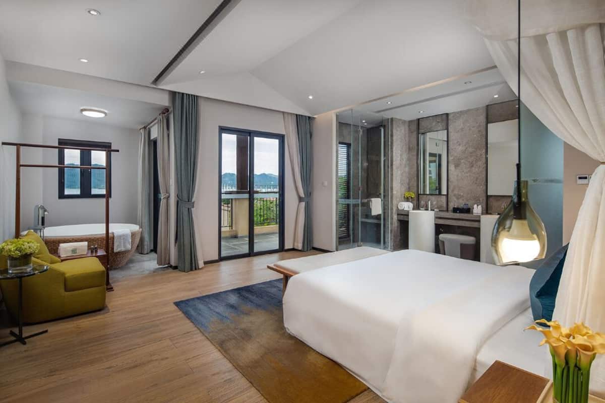 Habitación de hotel moderna con una cama grande, un escritorio, un baño con bañera y un balcón con vistas.
